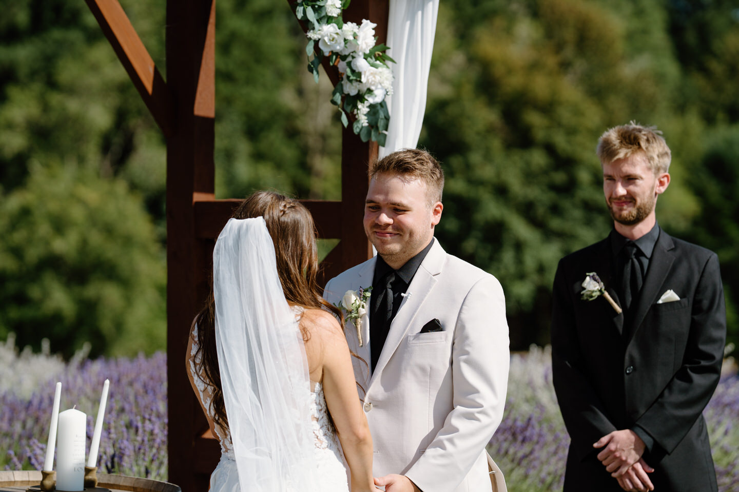 Groom smiles cheerfully at his bride in front of Lavender Farm wedding ceremony.