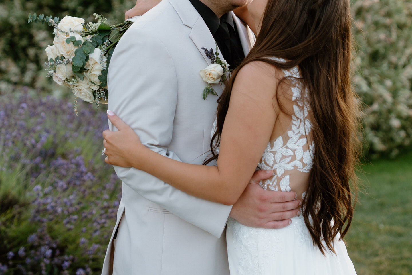 Close-up of bride and groom embracing with lace-back wedding gown.