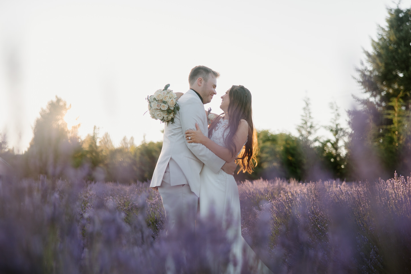 Bride and groom embracing in the blooming lavender field at sunset.