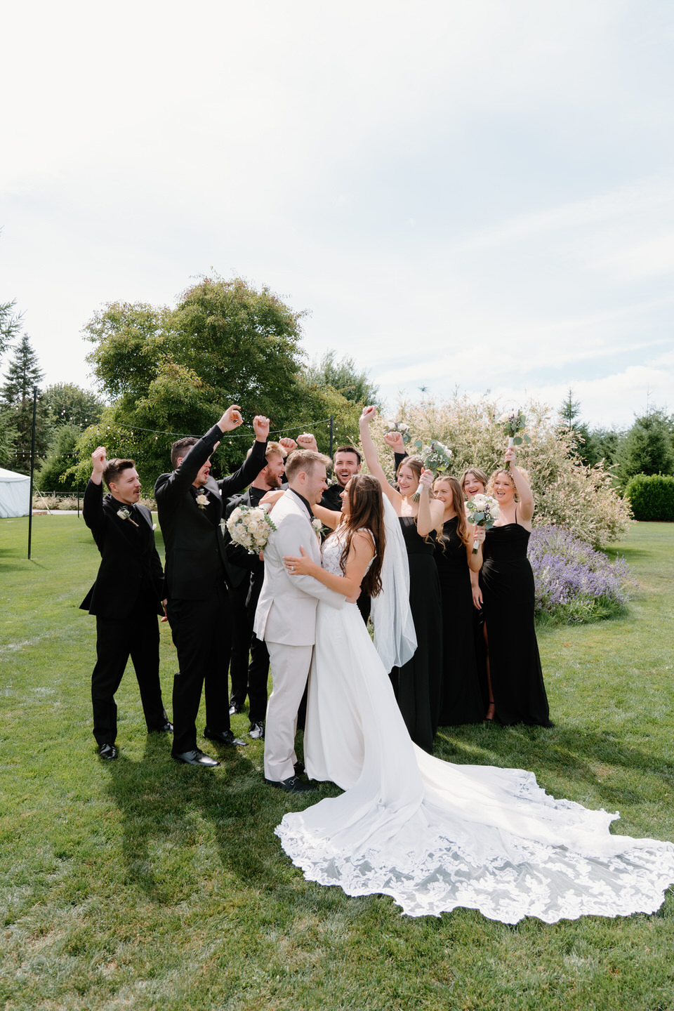 Full wedding party cheering and throwing their arms up around Hailey and Tyler.