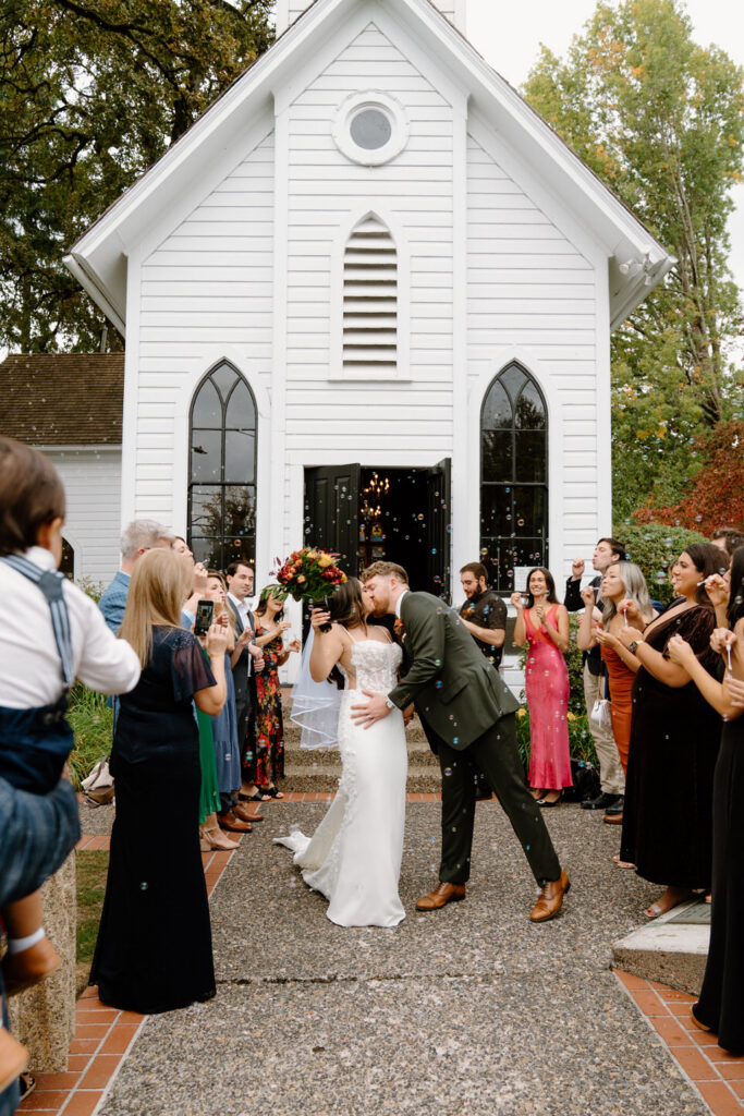 Bride and groom walk through a joyful guest tunnel outside the chapel after their romantic Oaks Pioneer Church wedding in Portland.
