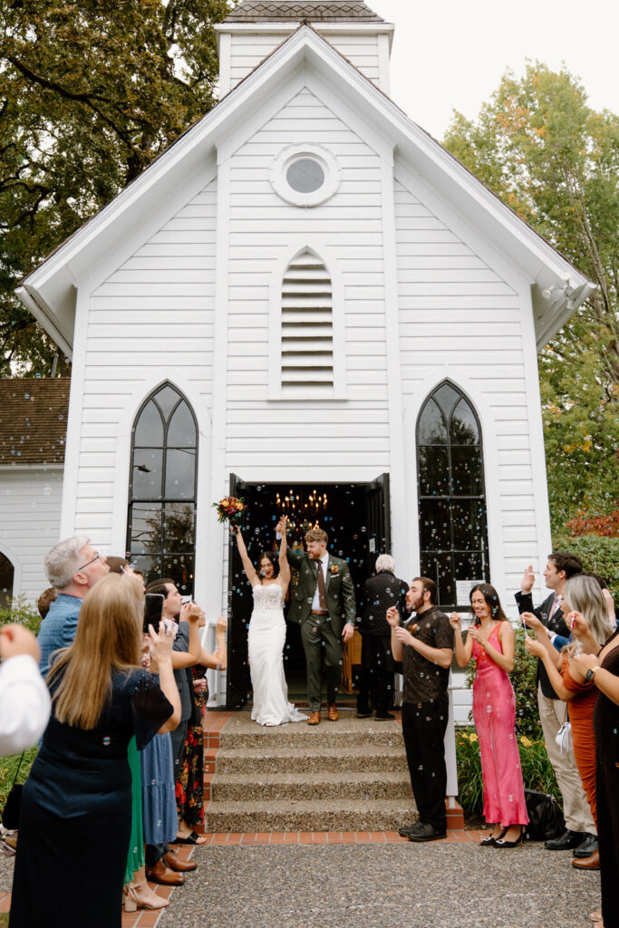 Guests blow bubbles and cheer as the newlyweds exit the chapel during their beautiful fall Portland wedding celebration.