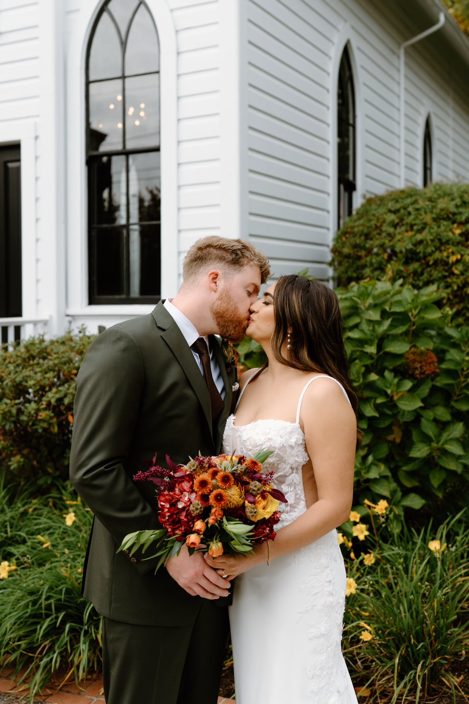 Bride and groom sharing a quiet kiss outside the chapel surrounded by greenery during their Oaks Pioneer Church wedding.