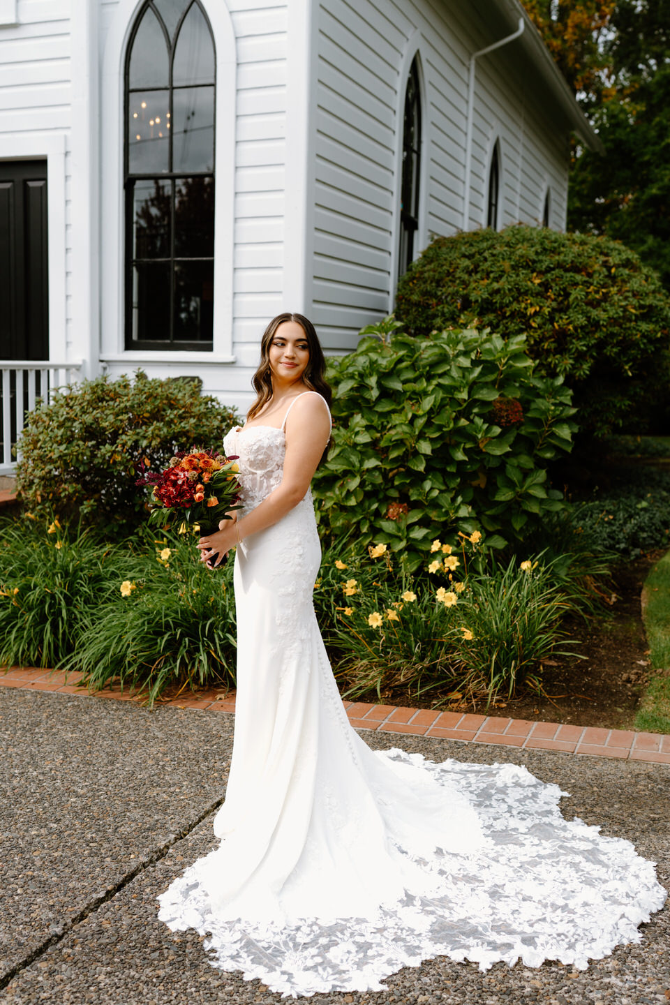 Bride standing outside the chapel holding a vibrant fall bouquet during a romantic Portland Oregon wedding portrait.