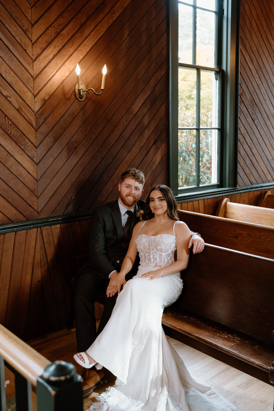 Bride and groom sitting together in wooden pews inside the chapel during their intimate Oaks Pioneer Church wedding.