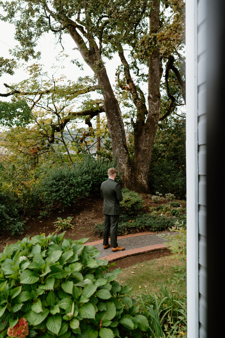 Groom standing beneath large trees in autumn colors before first look at an intimate wedding venue in Portland.