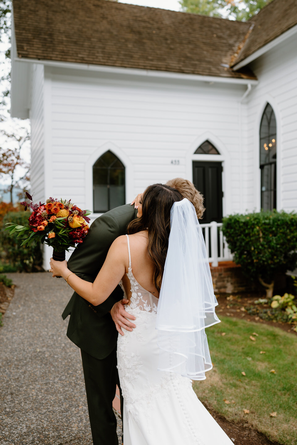 Bride hugging groom while holding a fall bouquet during portraits at their romantic Oaks Pioneer Church wedding.