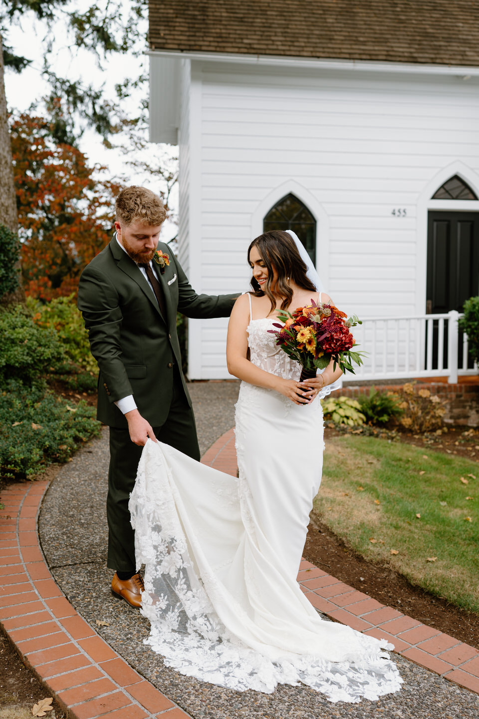 Groom gently lifting bride’s dress while walking along the garden path during a romantic Portland Oregon wedding.