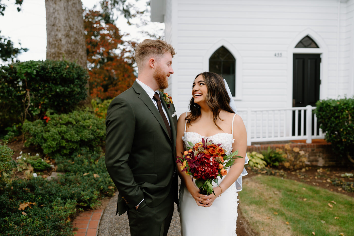 Couple smiling at each other while holding a colorful bouquet during their fall Portland wedding portraits.