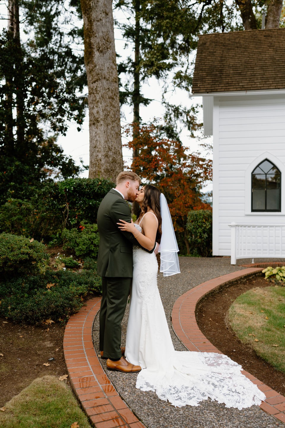 Bride and groom embracing along the curved path beside the chapel during their Oaks Pioneer Church wedding portraits.