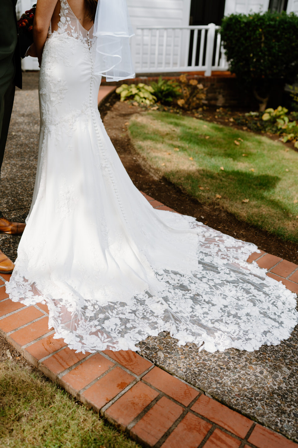 Lace train of bride’s dress flowing over brick walkway outside the chapel during a fall Portland wedding.