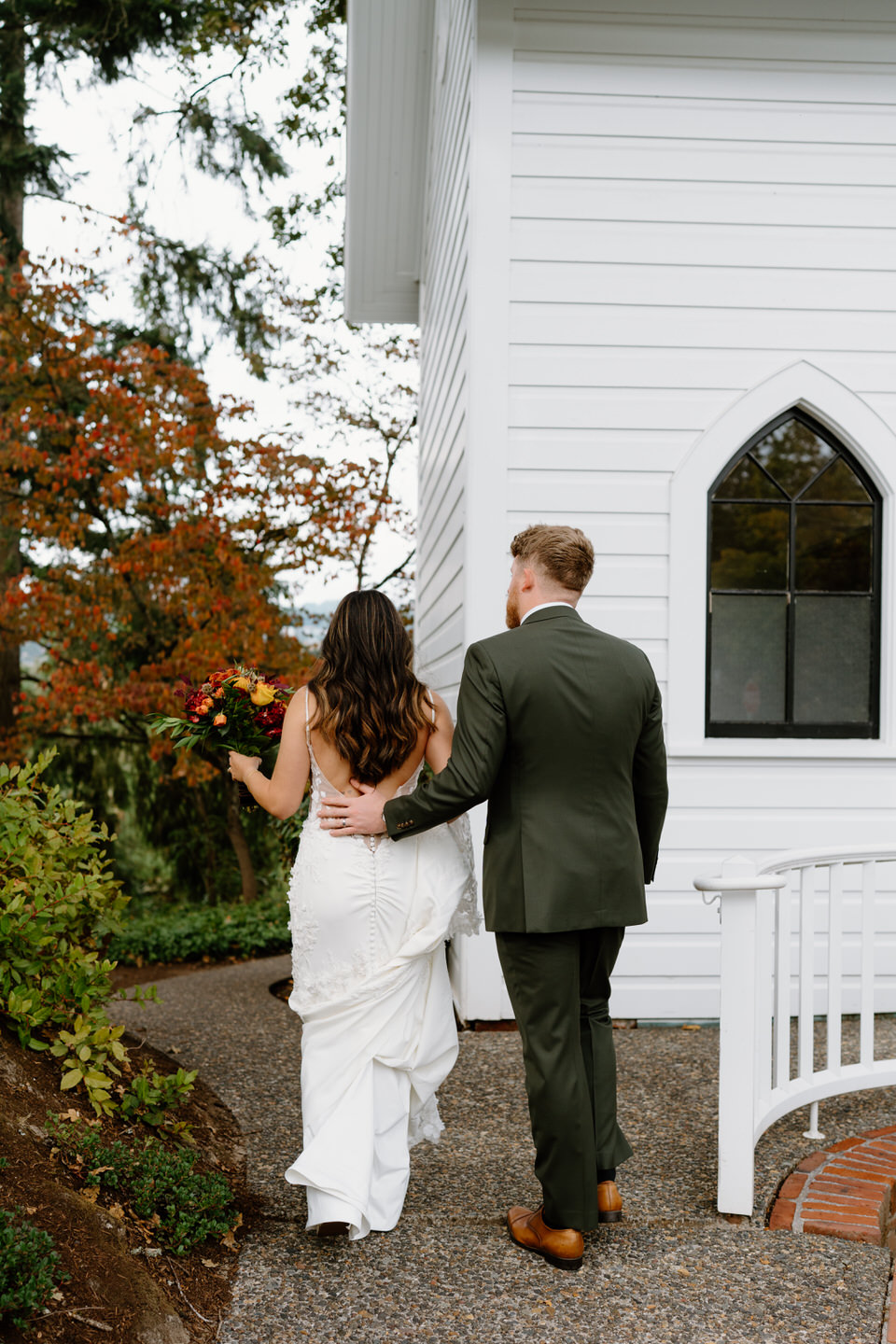 Bride and groom walking away together beside the chapel during a romantic Portland Oregon wedding portrait.