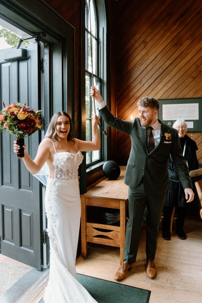 Bride and groom ring the chapel bell smiling and celebrating with guests during their joyful Oaks Pioneer Church wedding ceremony in Portland.