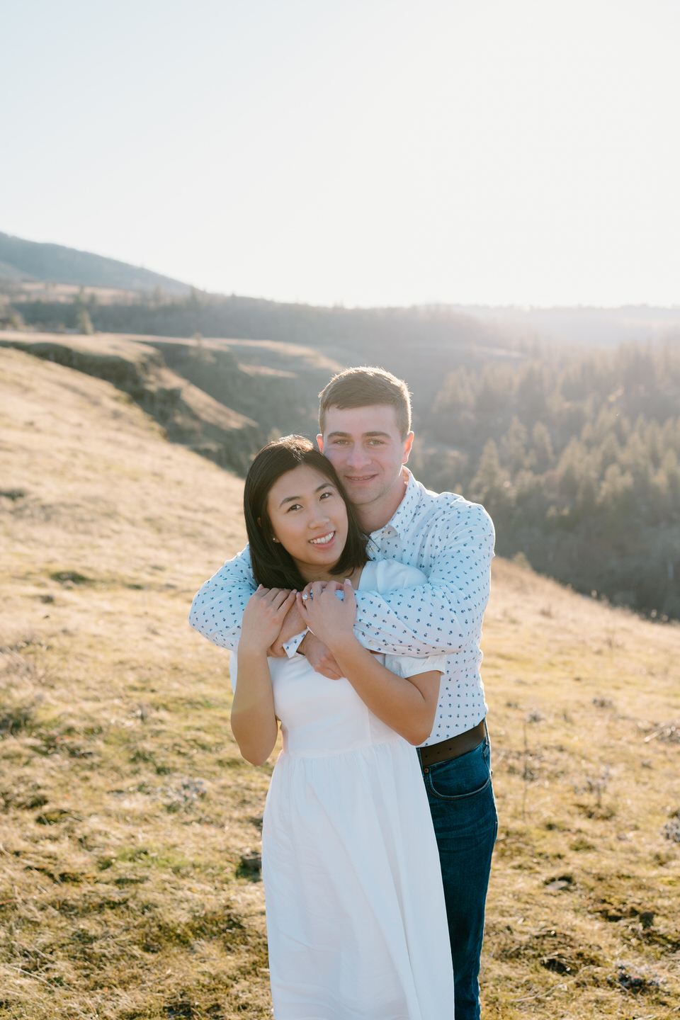 Alex wraps his arms around Min as they smile at the camera during their winter engagement session at Rowena Crest.