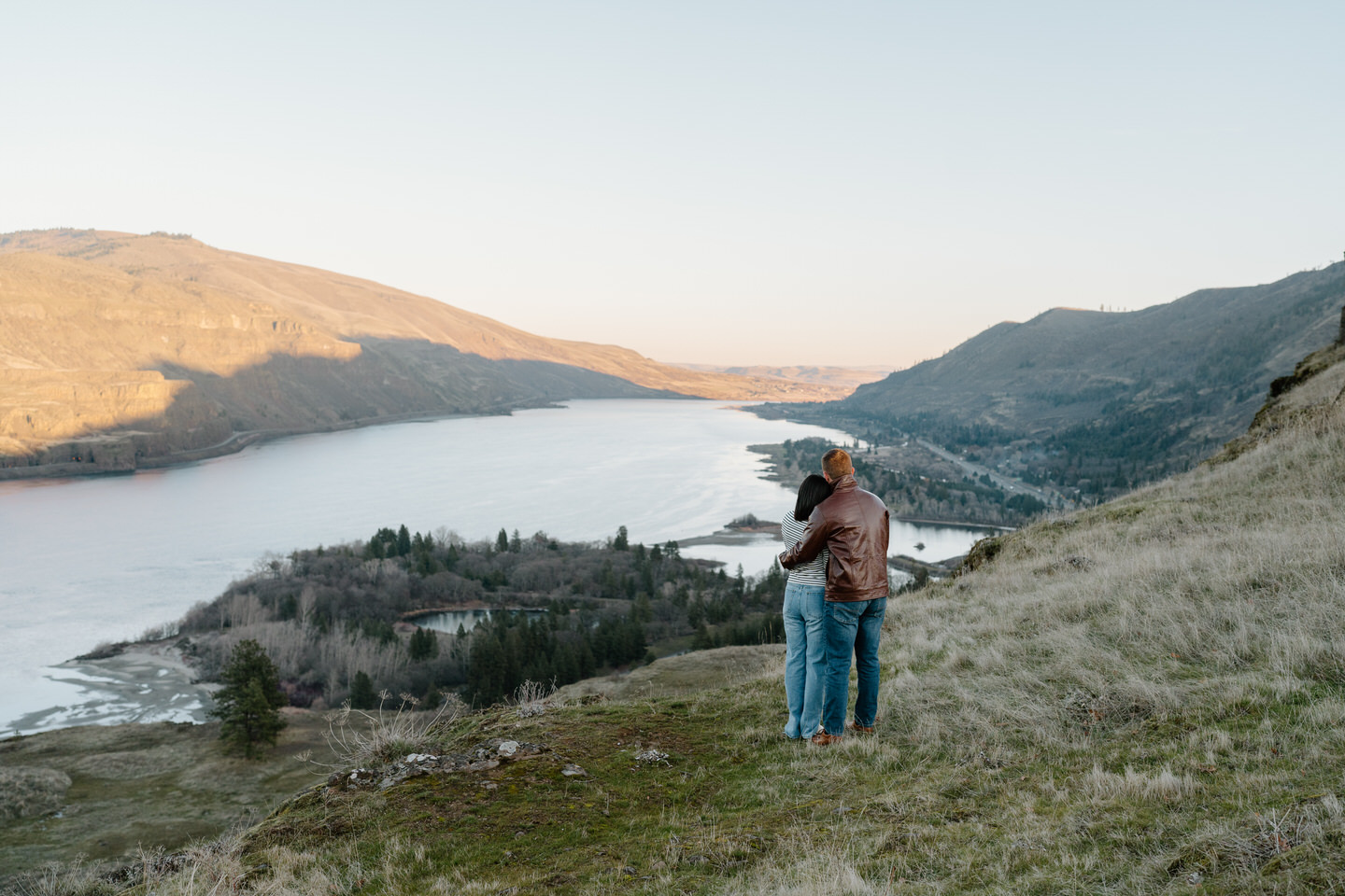 Couple with their arms around each other looking over the Columbia River Gorge during Rowena Crest engagement photos.