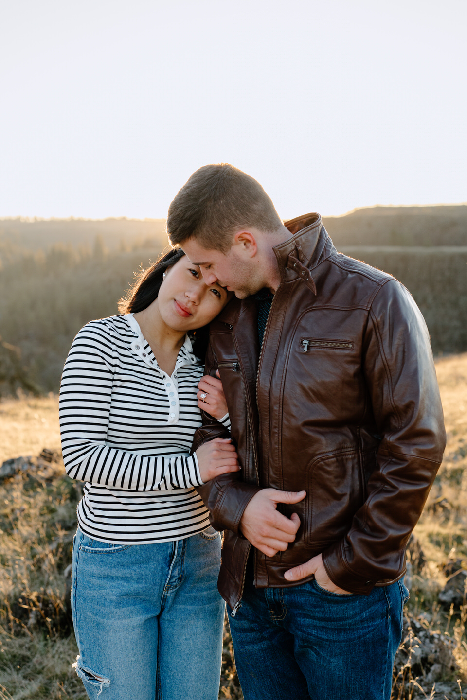 Min clutches Alex's arm and leans her head on his shoulder while he looks down at her.