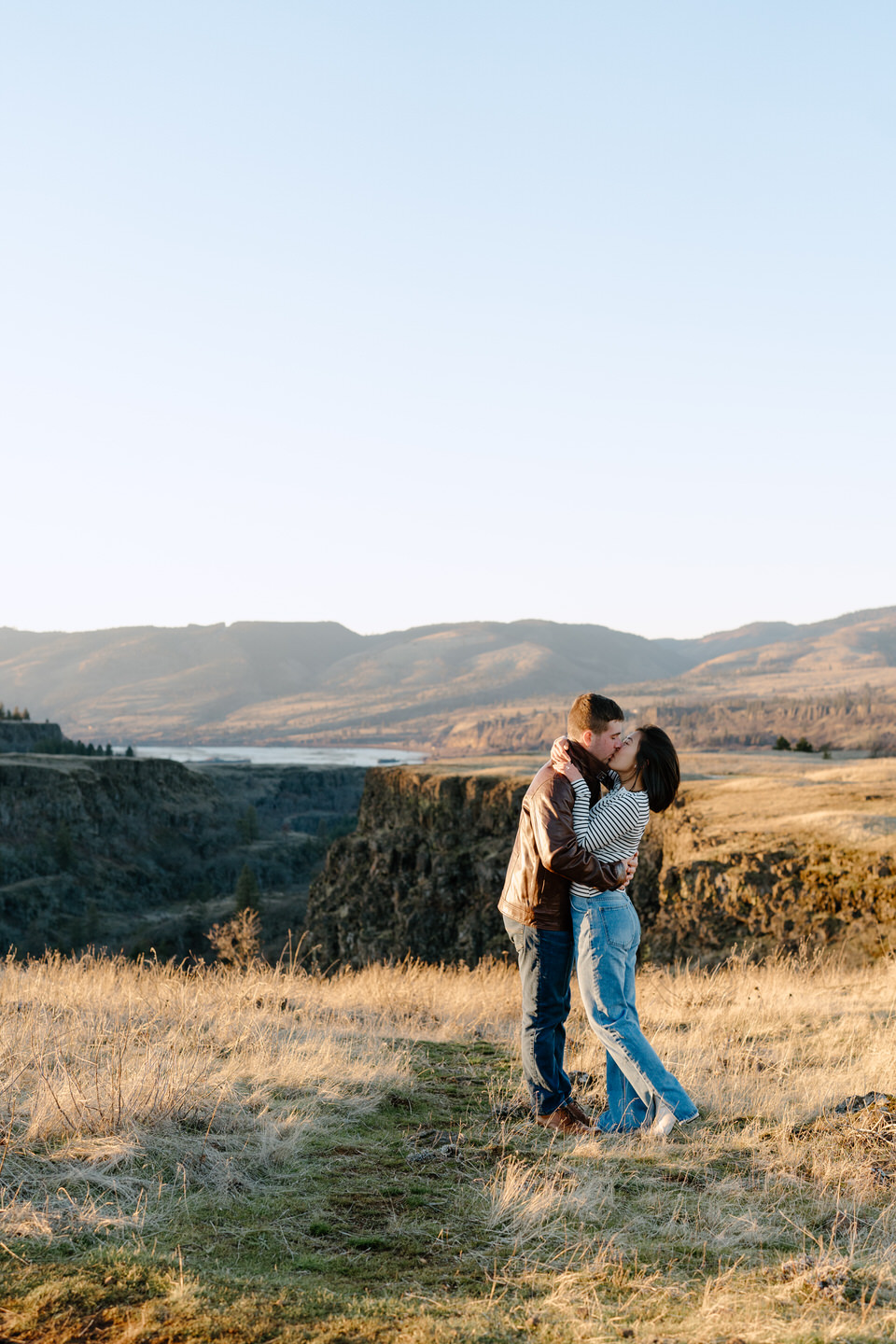 Couple shares a kiss under glowing golden light in the winter at Rowena Crest.