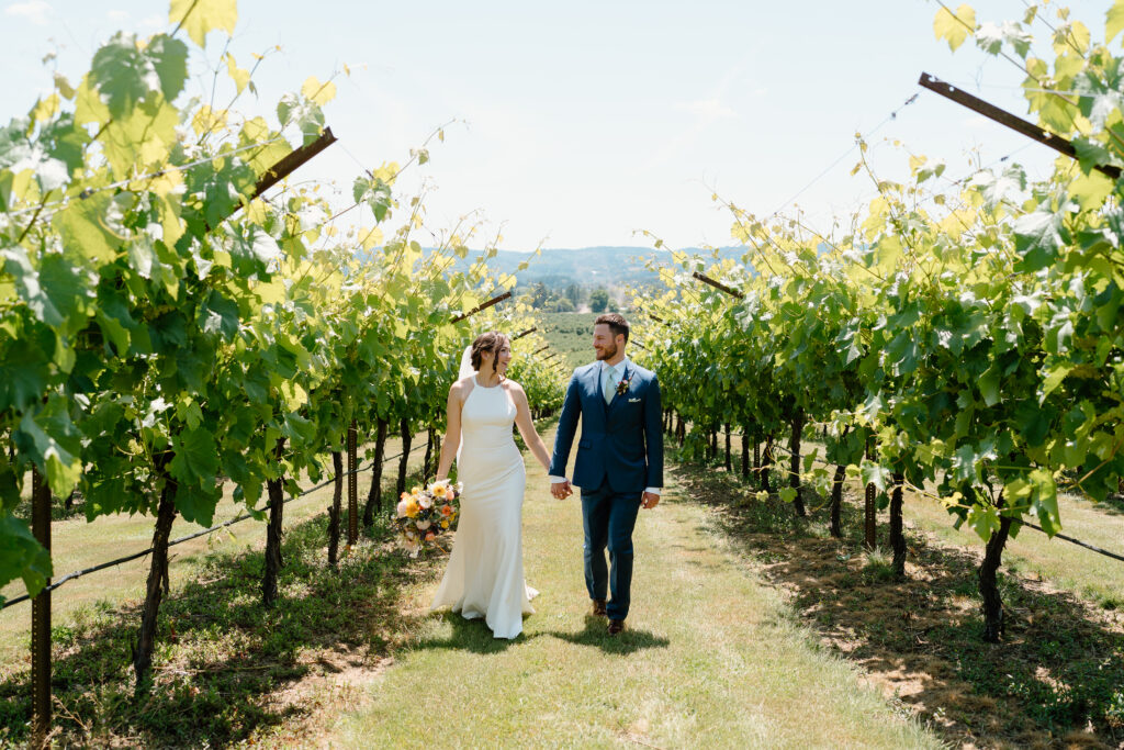 Bride and groom in grassy vineyard at Scholls Valley Lodge, holding hands and walking on their wedding day