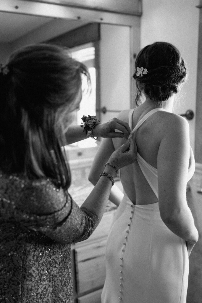 Mom buttoning bride's dress on wedding day