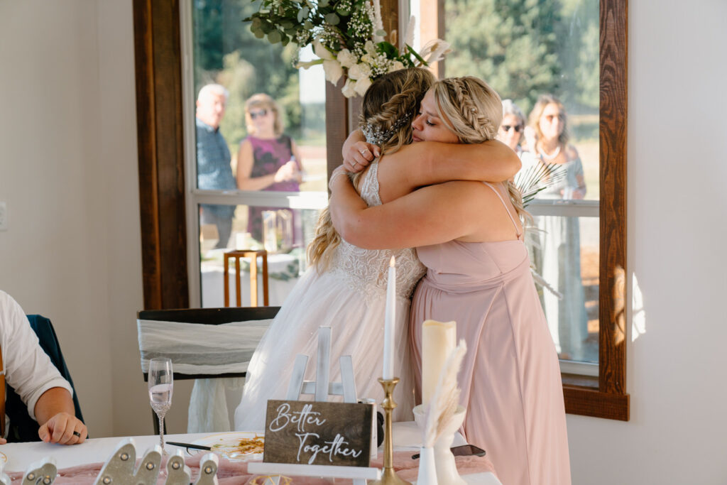 Bride and maid of honor hugging during toasts at the barn wedding