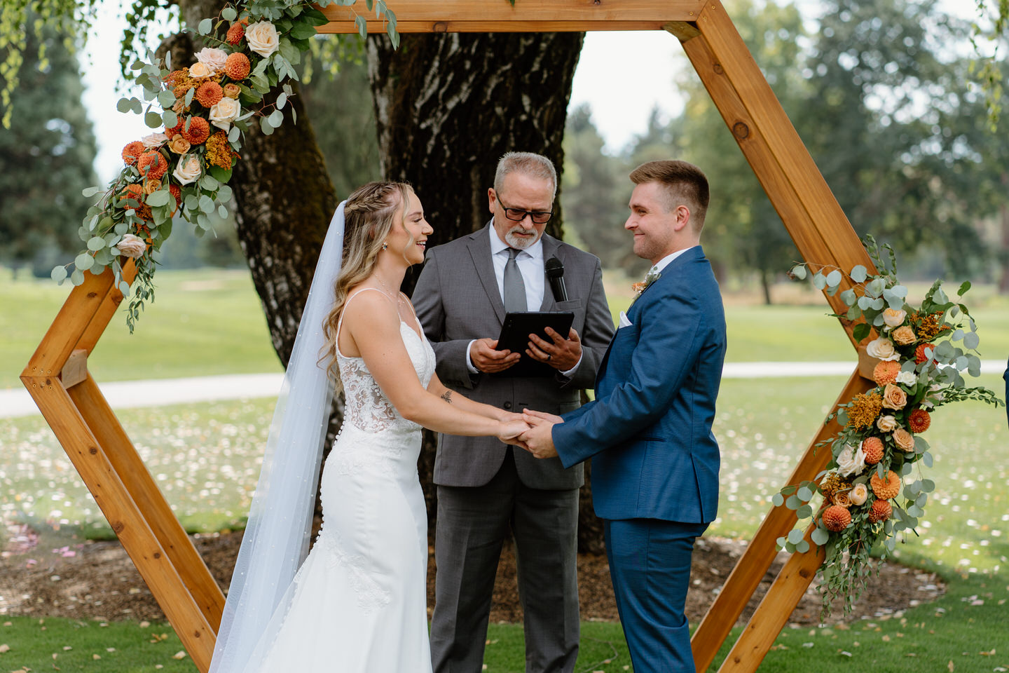 Bride and groom holding hands during wedding ceremony with hexagonal arch