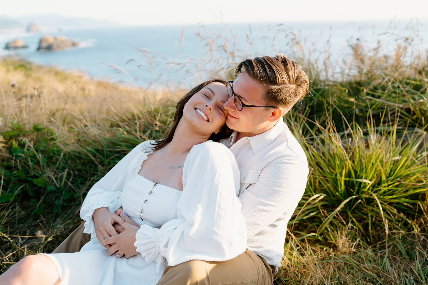 couple sitting in tall grass for oregon coast engagement photos at ecola state park