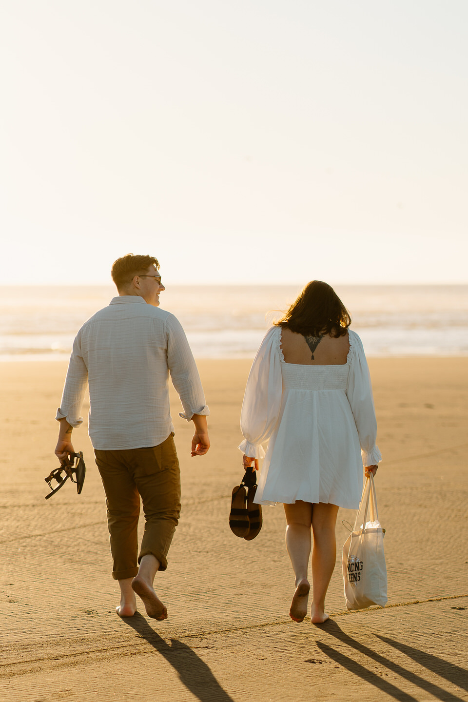 candid engagement photos at the beach with couple holding belongings as they walk