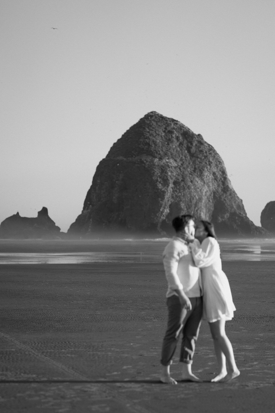 black and white photo of haystack rock with couple kissing in front of it