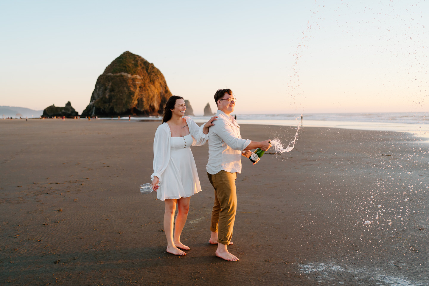 couple spraying champagne in front of haystack rock on the oregon coast