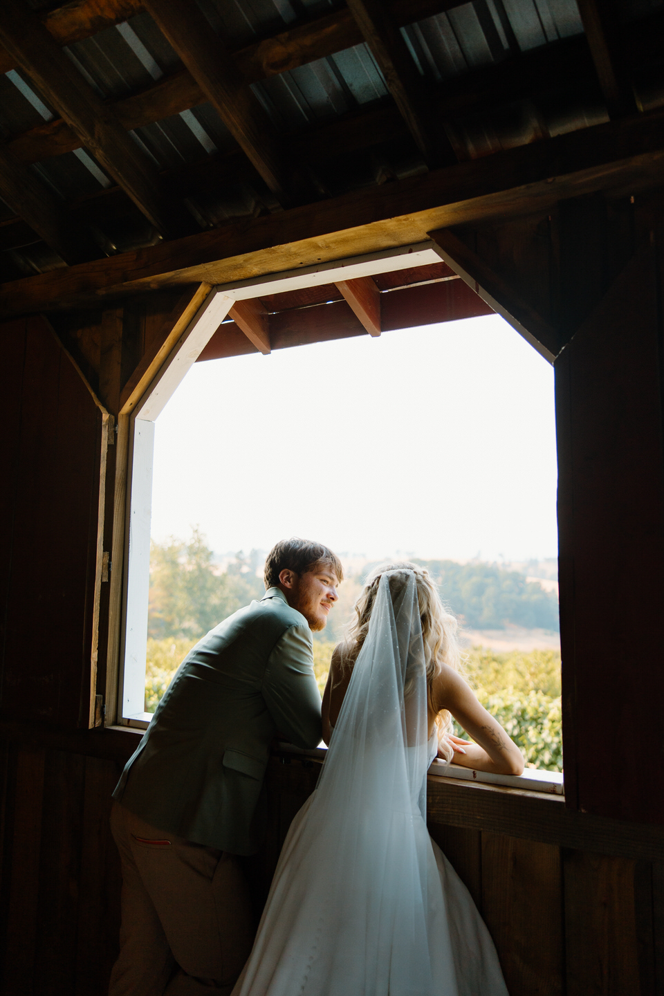 bride and groom leaning out of their rustic barn wedding window