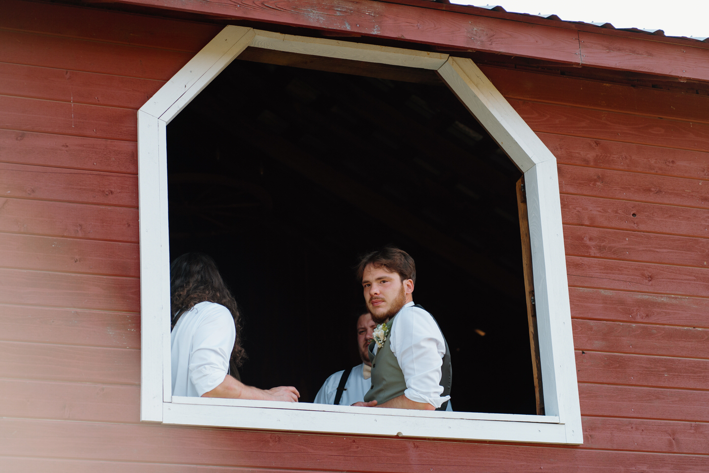 groom looking out barn window at wedding