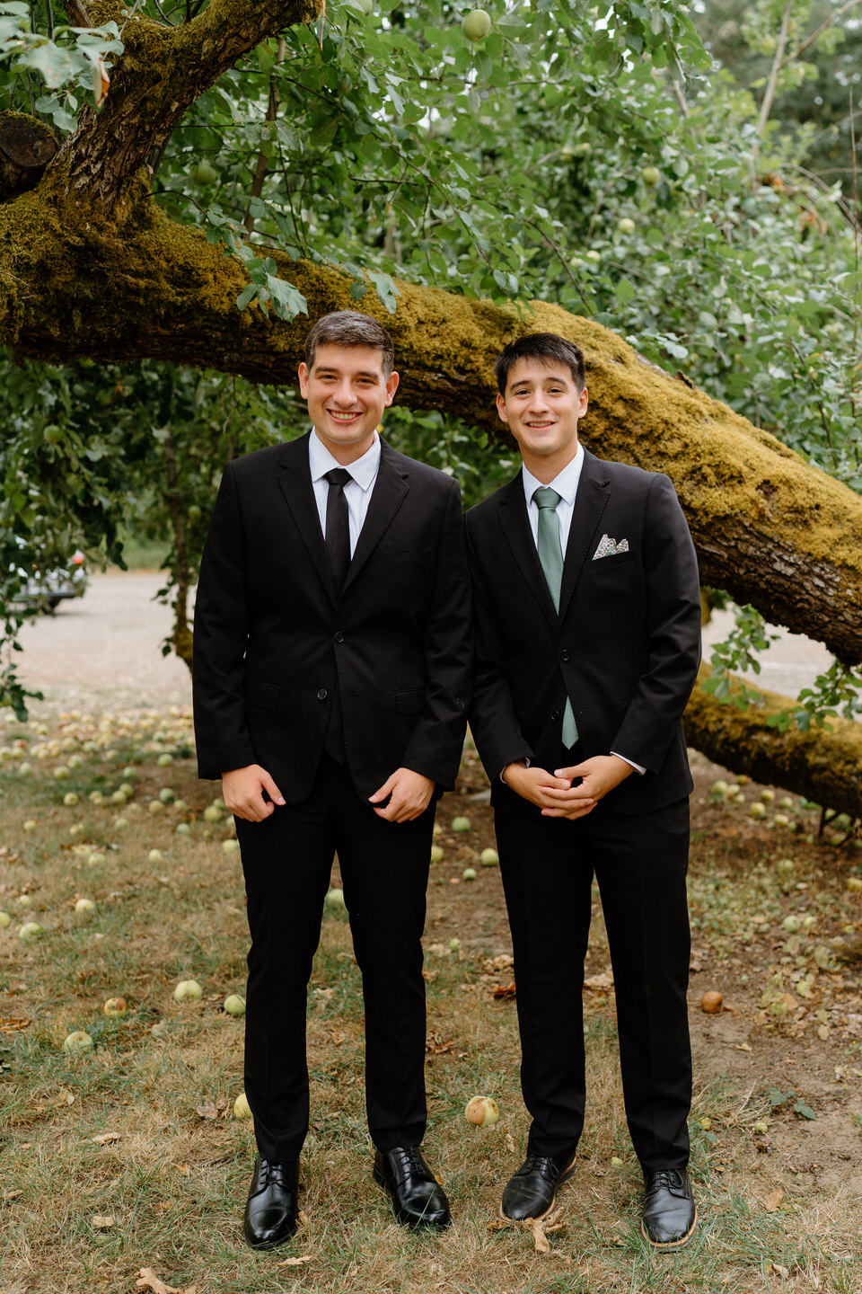 Groom and brother stand together in front of Oak Tree before Navarra gardens wedding.