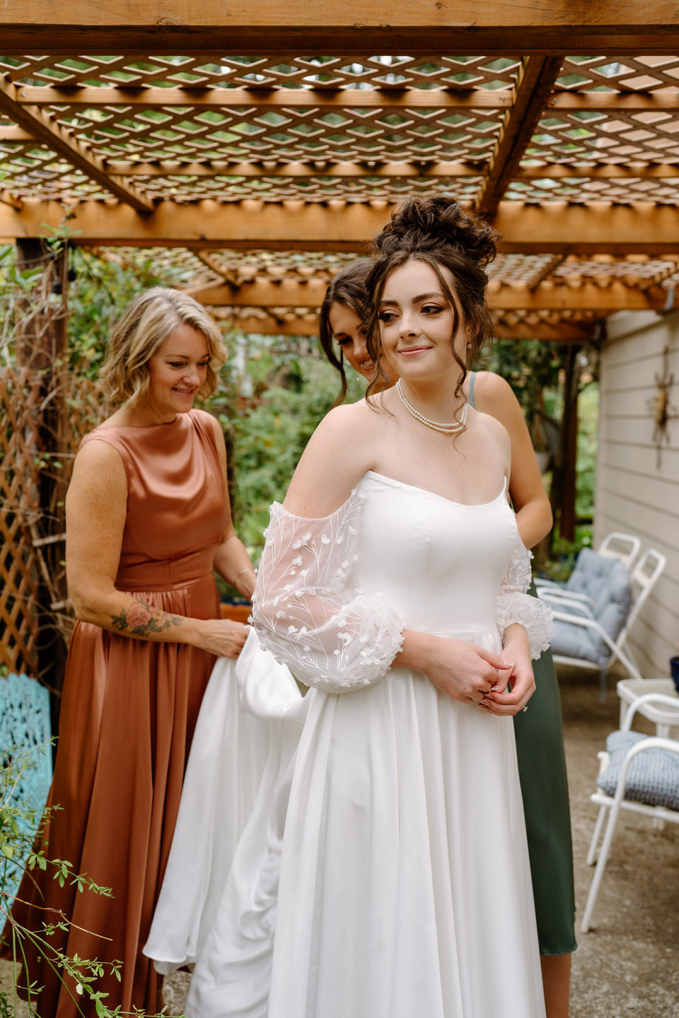 The mother of the bride and sister of the bride help zip the bride into her dress at Navarra Gardens.