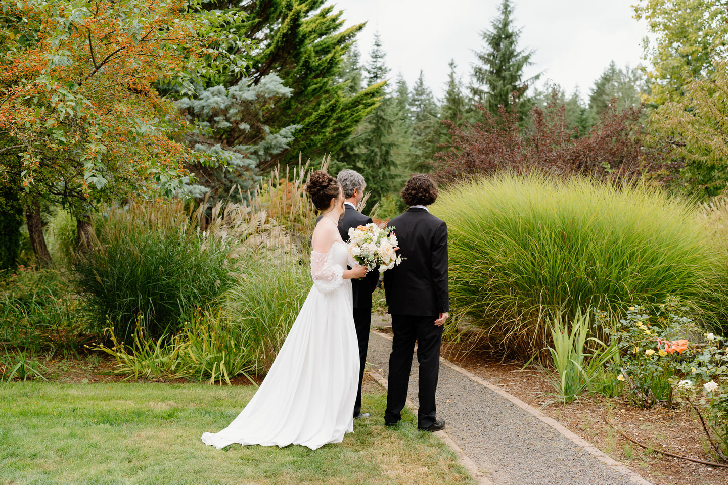 Bride taps her dad and brother on the shoulder for a first look in the garden on her wedding day.