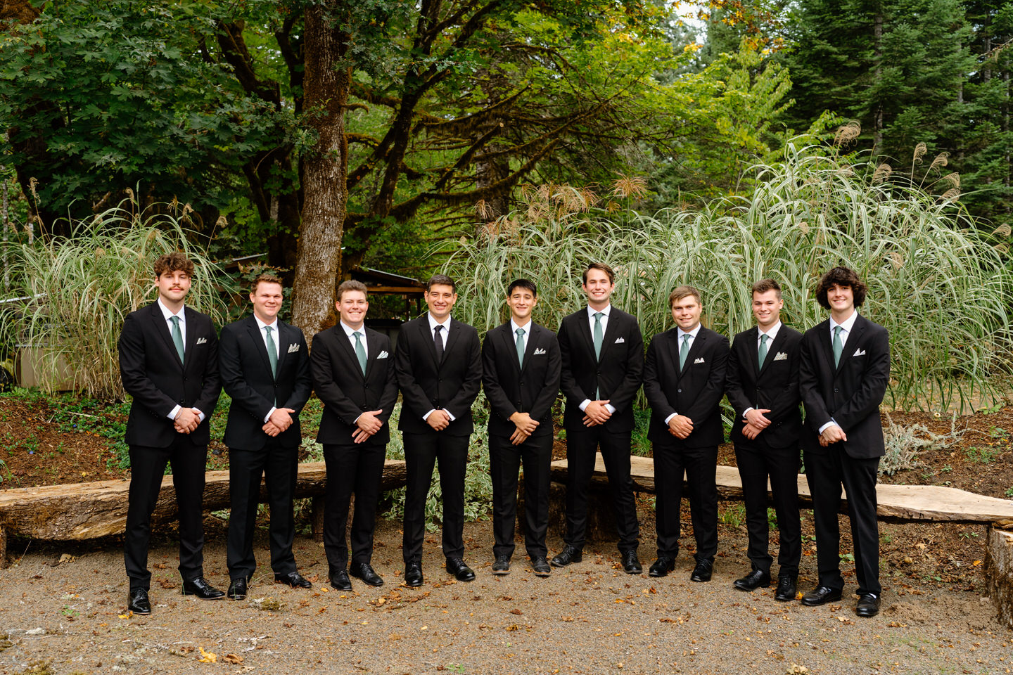 Groomsmen stand in a line in front of foliage for Navarra Gardens wedding.