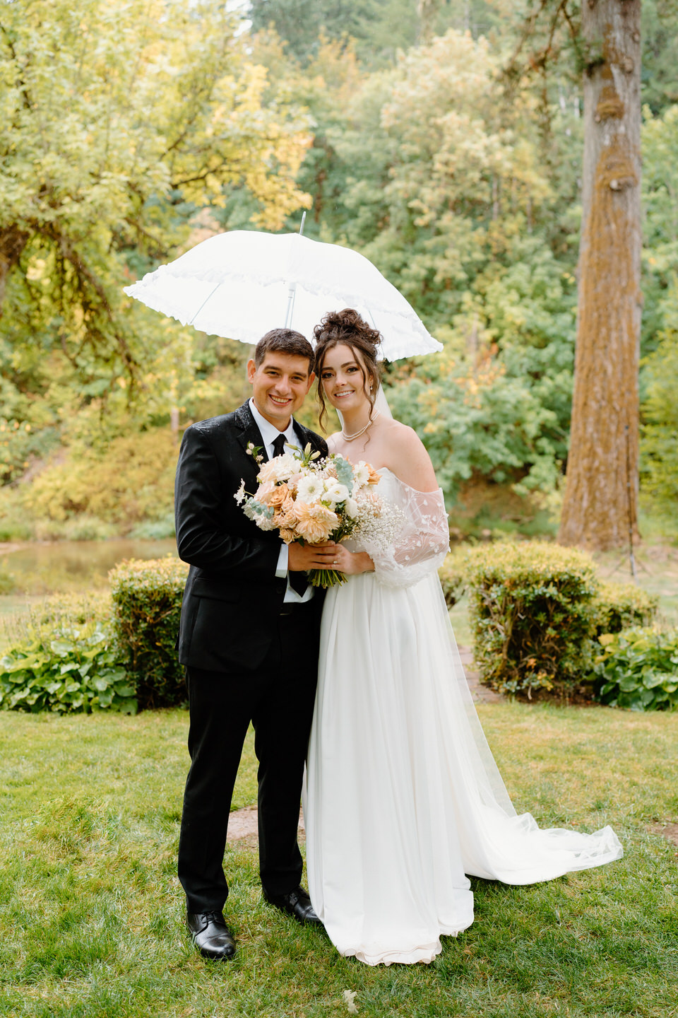 Bride and groom pose under an umbrella during a rainy wedding ceremony in Oregon.