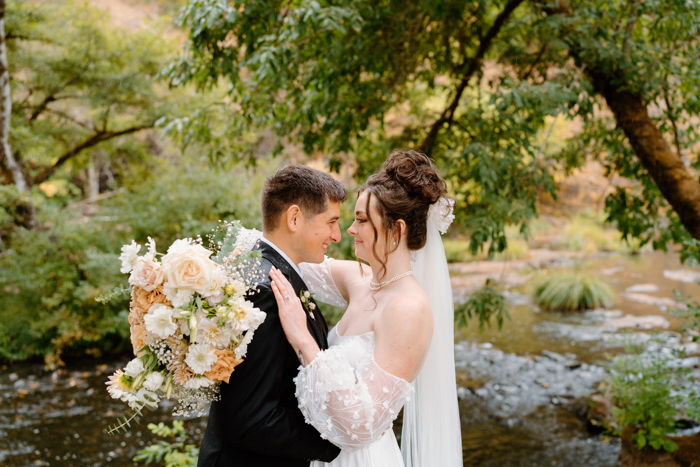 Bride and groom look at each other with her fall-inspired bouquet in her hand.