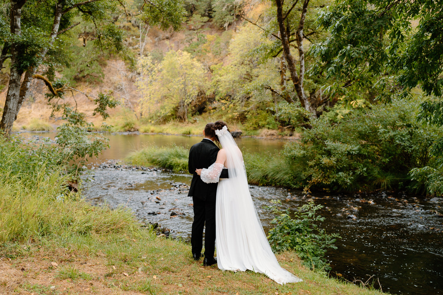 Bride and groom face away from the camera to look at the river that flows next to Navarra Gardens.