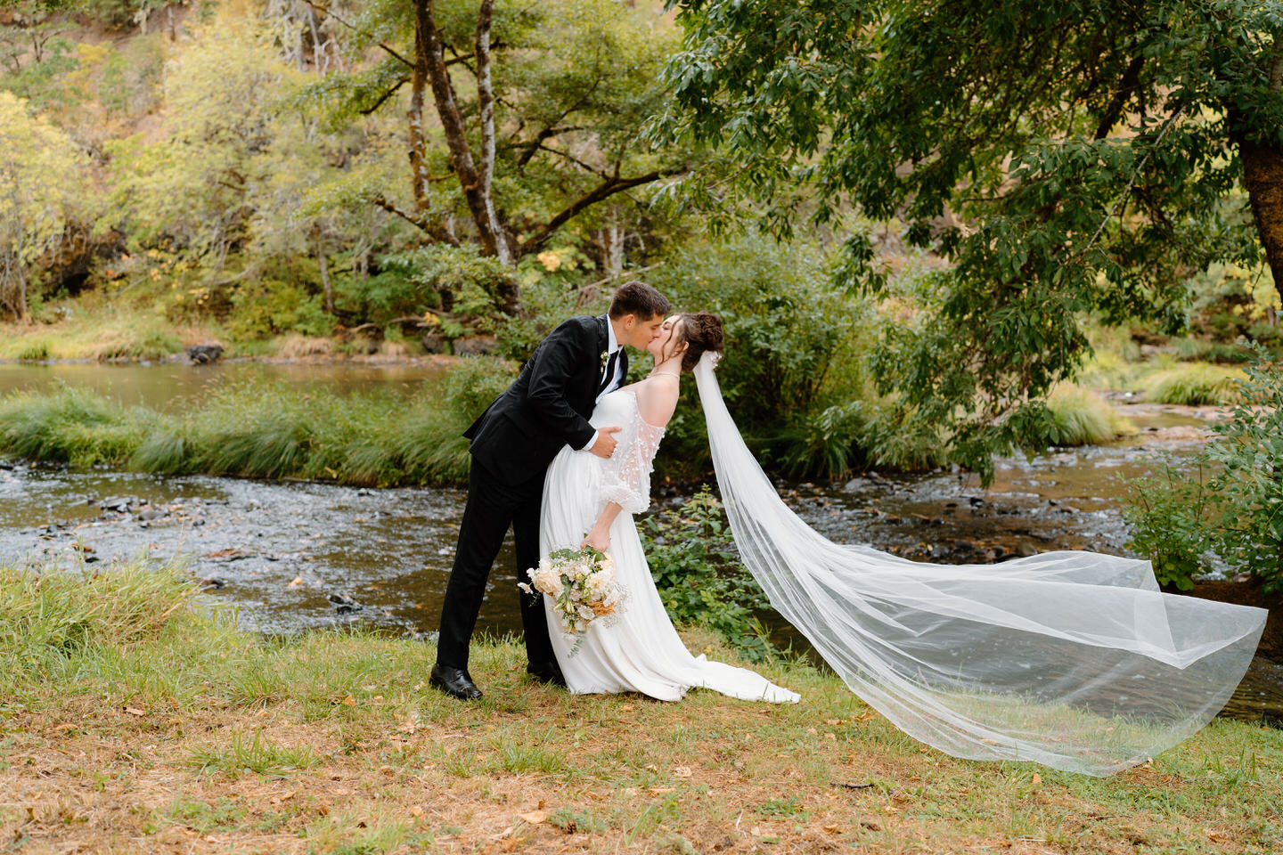 Bride and groom kiss in front of the river at Navarra Gardens during a fall wedding.