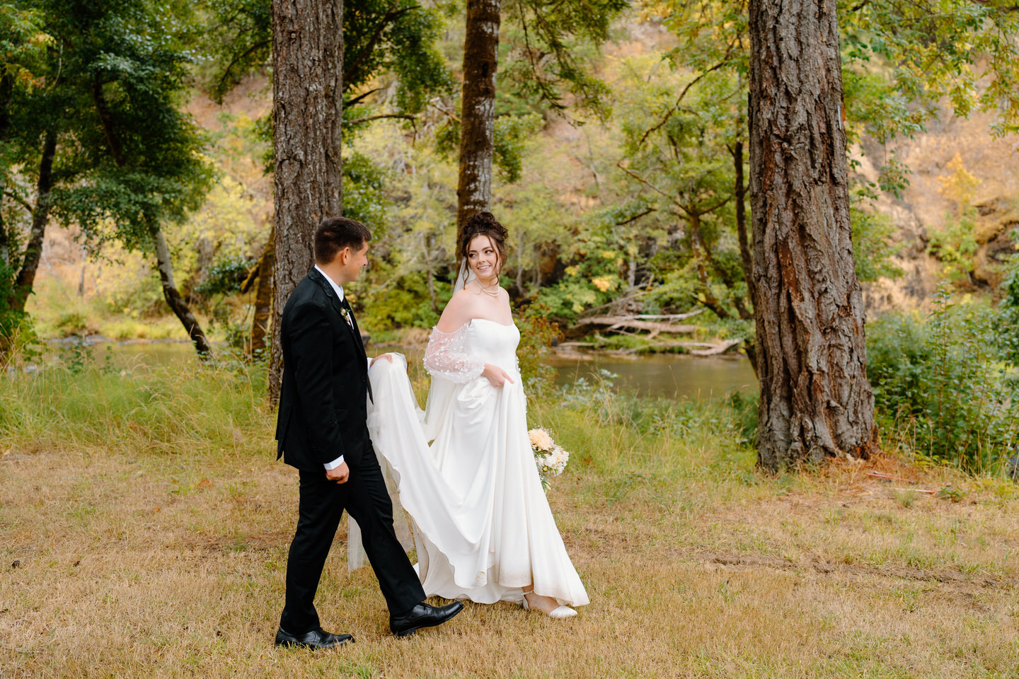 Couple walks along the river on their wedding day. It's raining, but everything looks beautiful.