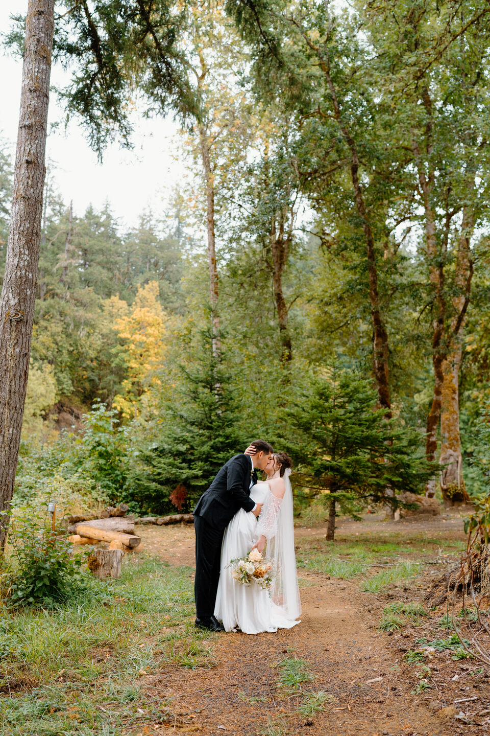 Bride and groom kiss in the forest on a fall wedding day in Oregon.