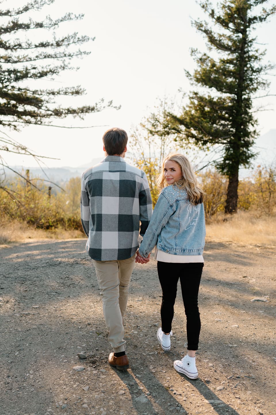 Couple walks away from camera and woman looks back wearing her bridal denim jacket with pearls.