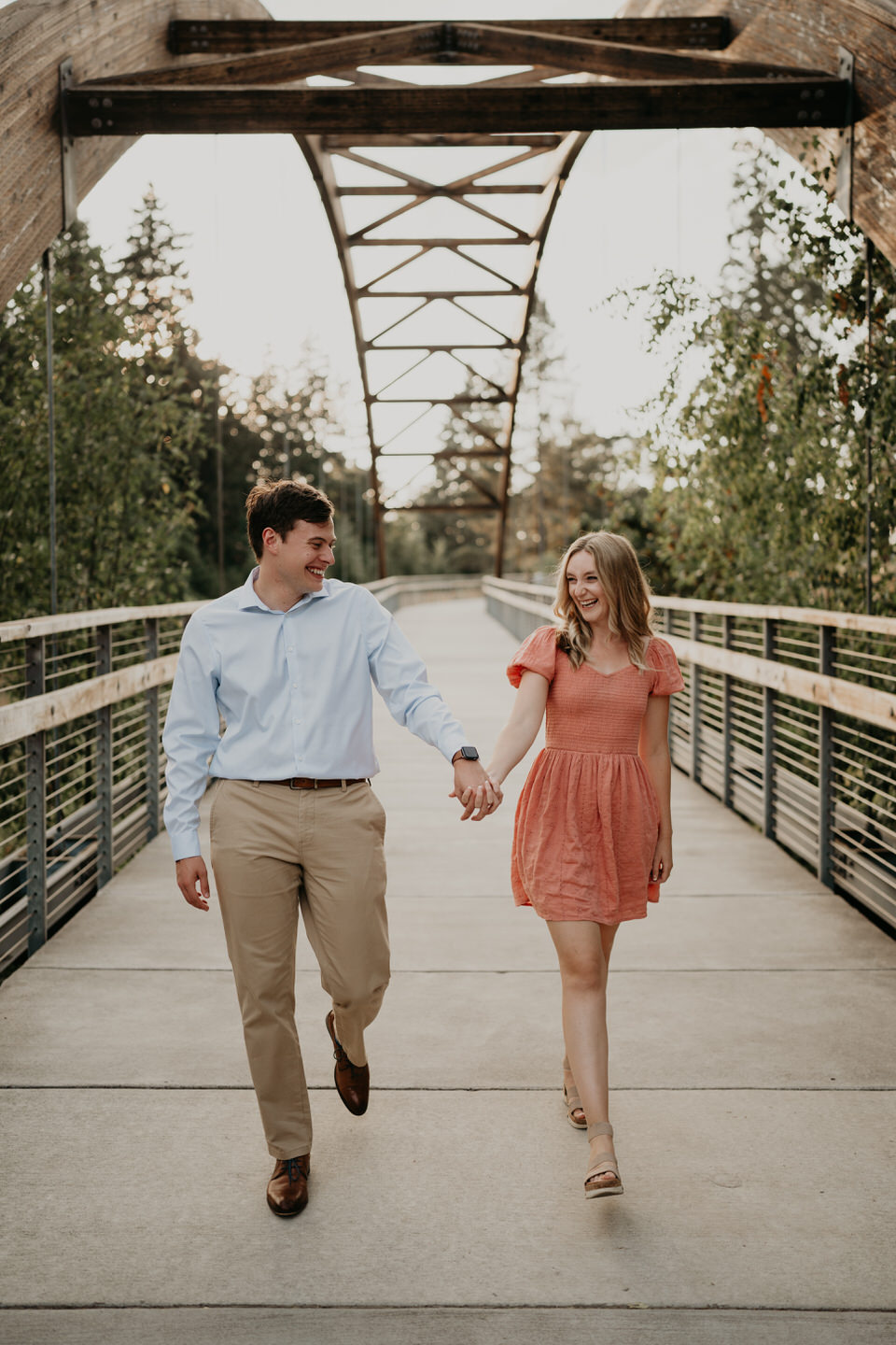 Oregon engagement photo locations in Hillsboro, Oregon. Couple holds hands and walks across pedestrian bridge.