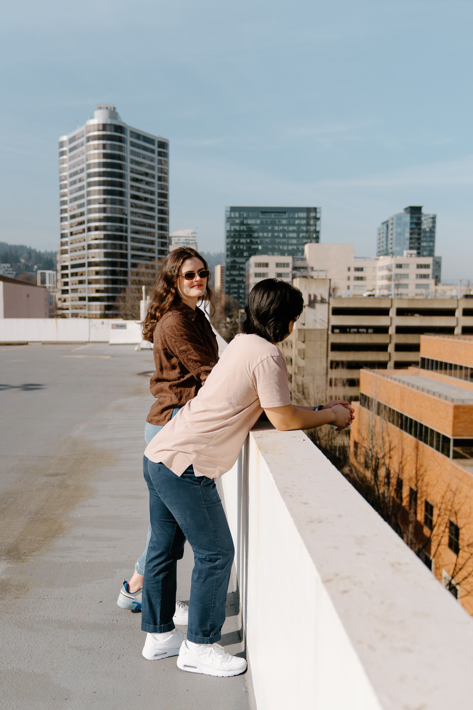 Editorial-style engagement photos in Portland, Oregon on a rooftop parking gargage. Man leans over ledge as woman looks over him.