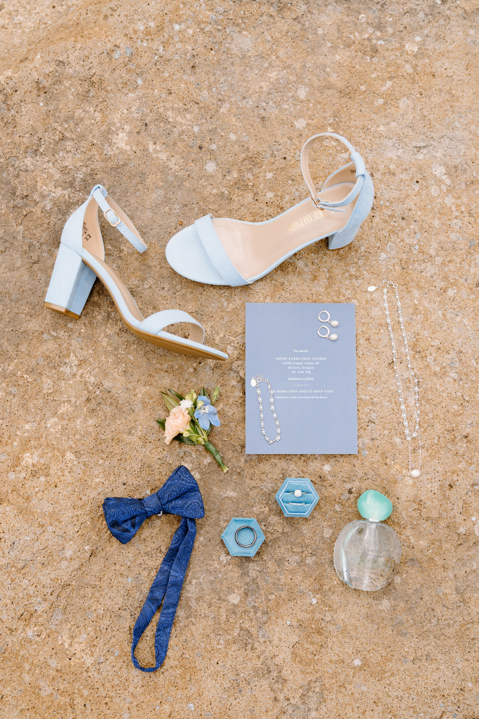 Detail photo of bride's shoes, perfume, and rings with groom's bowtie and florals. 