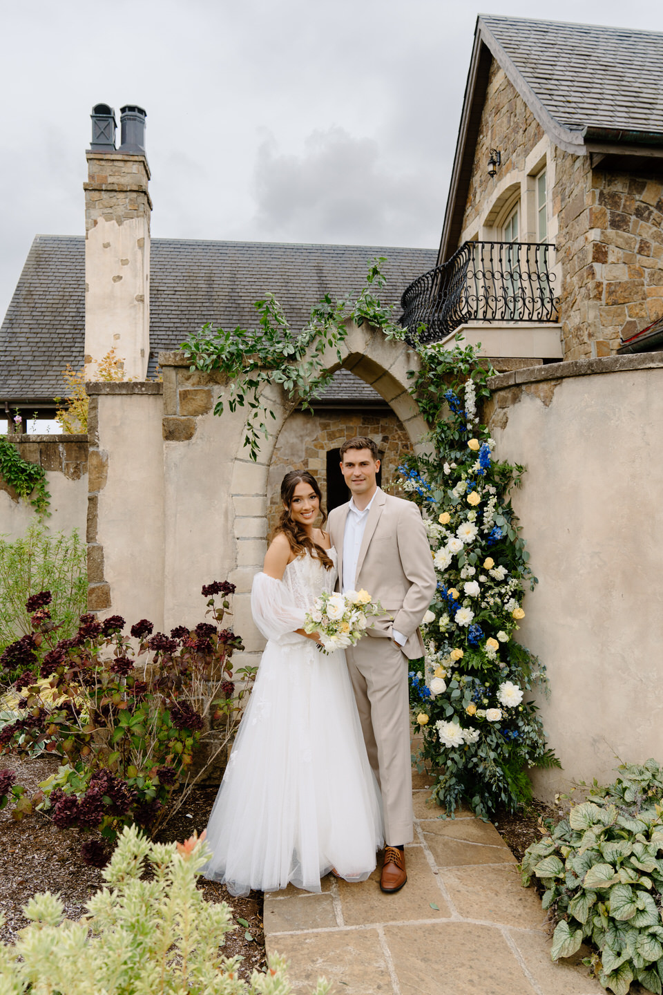 Couple standing under stone archway at Chateau de Lis