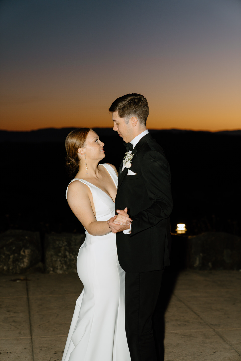 Bride and groom share their first dance with a sunset behind them