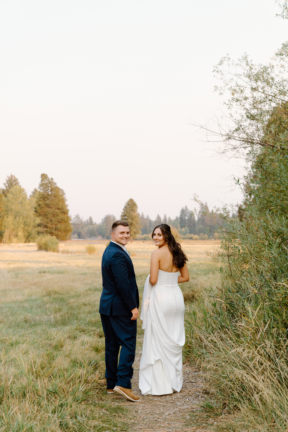 The bride and groom stroll at sunset in Black Butte Ranch, their October wedding glowing in the warm golden light.