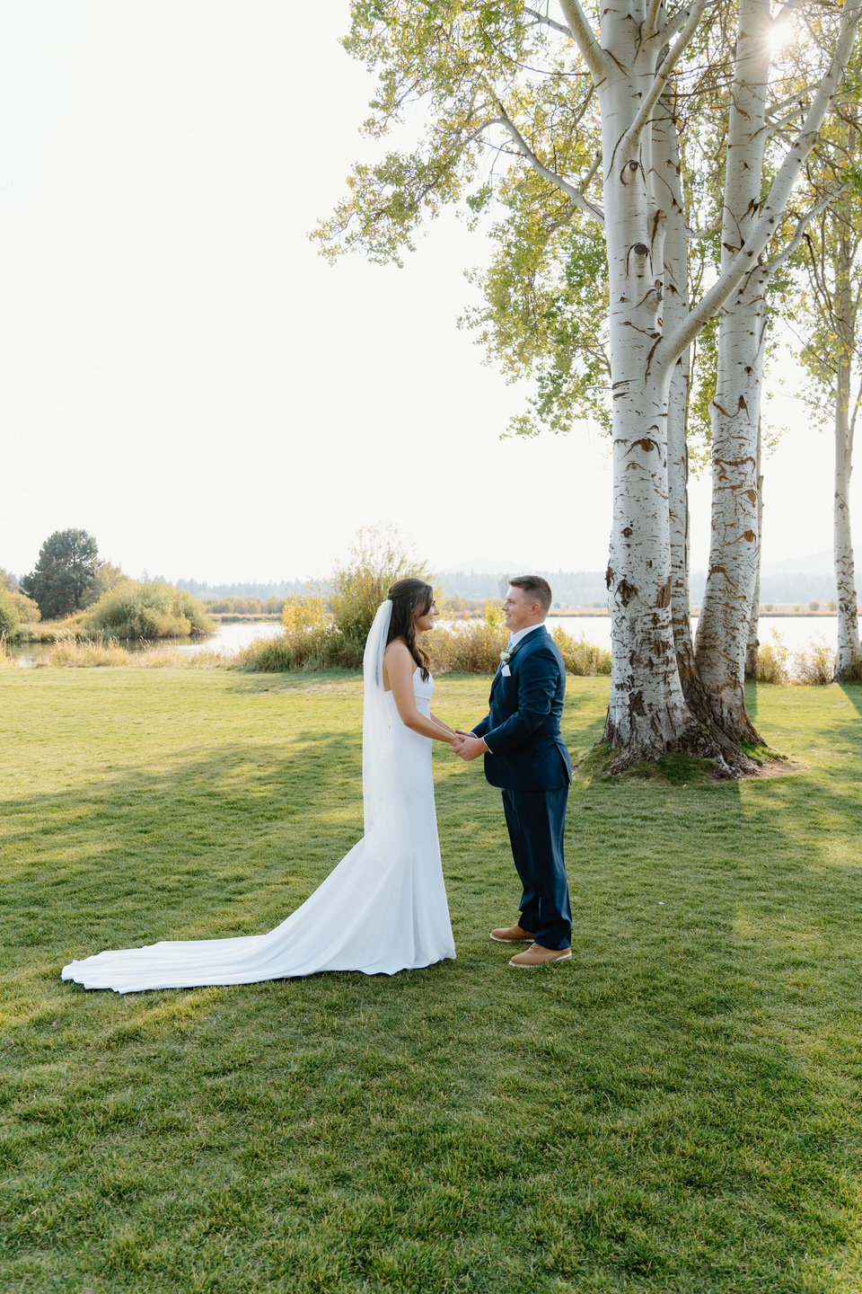 Bride and groom share a tender first look at Black Butte Ranch, with the sun glowing over the lake behind.