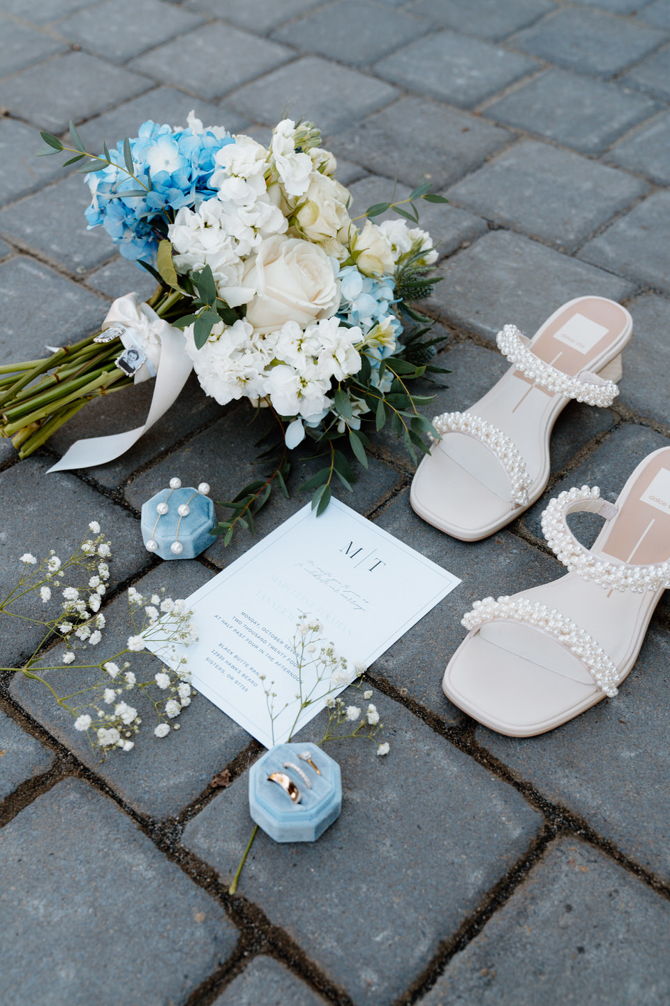 Wedding rings, a floral invitation, delicate flowers, and elegant shoes arranged together, capturing timeless details of the day.